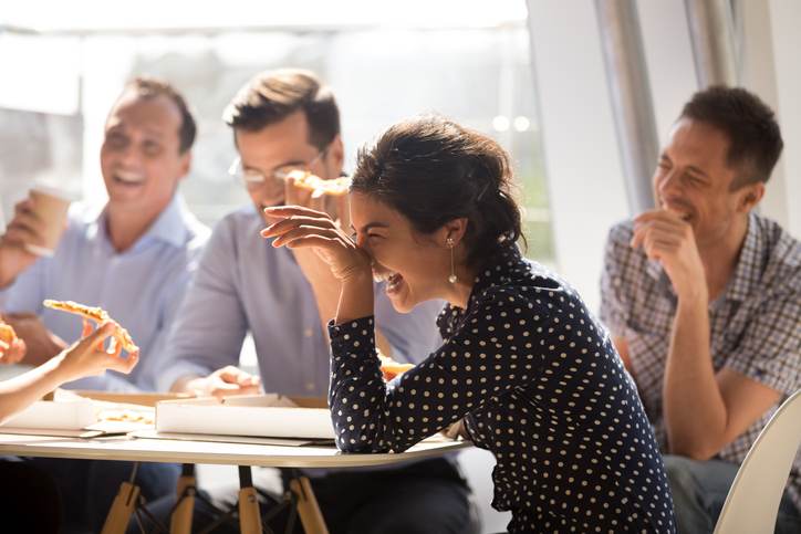 Indian woman laughing eating pizza with diverse coworkers in office Indian woman laughing eating pizza with diverse coworkers in office